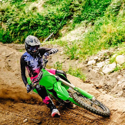 motocross rider wearing pink black and white sidi boots on green motorbike on dirt trail
