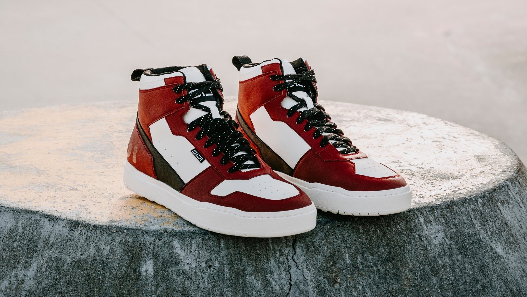 Red and white high-top motorcycle trainers on a textured surface with a neutral background